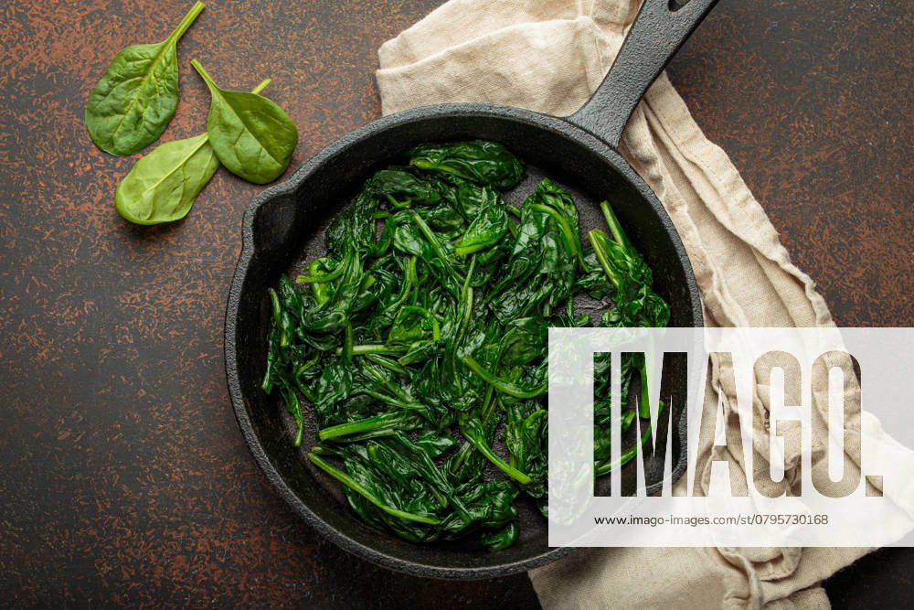 Gesunder gedünsteter Spinat in gusseiserner Pfanne auf braunem rustikalem Hintergrund von oben gesehen Freshly steamed spinach leaves are served in a cast iron pan, a nutritious and flavorful side dish or ingredient for healthy meals
