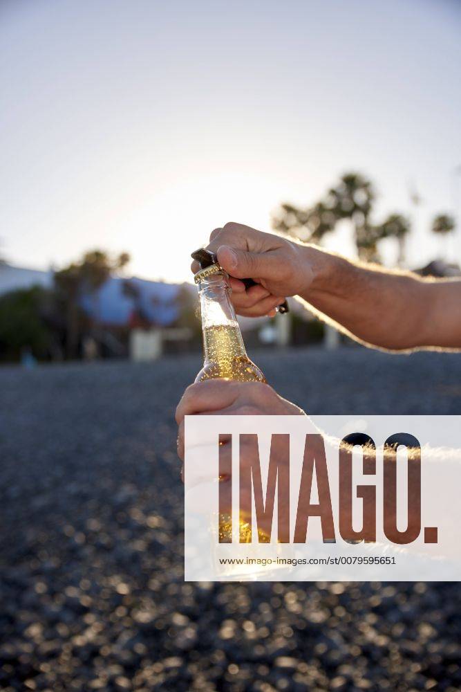 Man s hands opening beer bottle on the beach model released Symbolfoto PACF00029