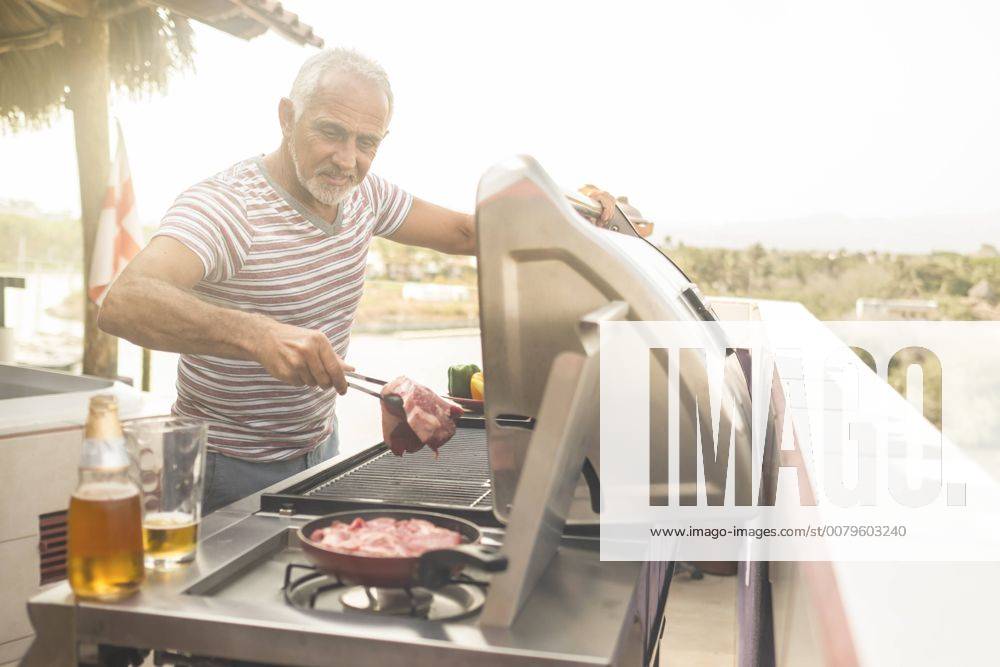 Mature man grilling steaks on a gas grill on his penthouse terrace model released Symbolfoto property released ABAF02158