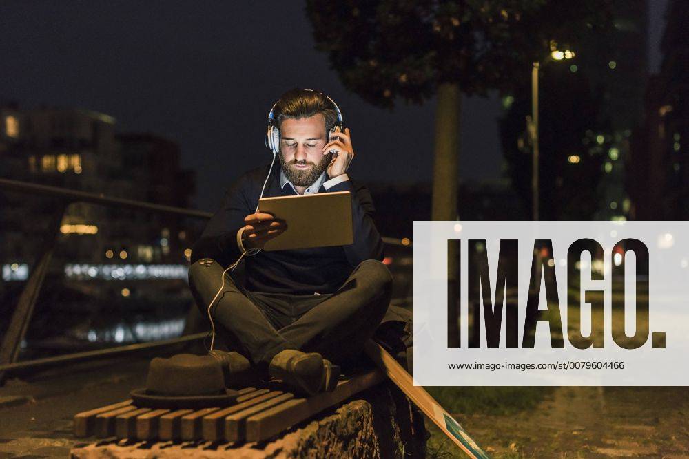 Young man with tablet and headphones in the city at night model released Symbolfoto UUF10891