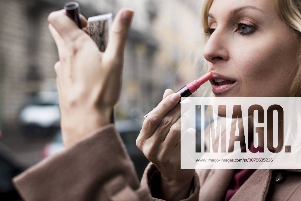 Businesswoman applying lipstick outdoors model released Symbolfoto MAUF01111