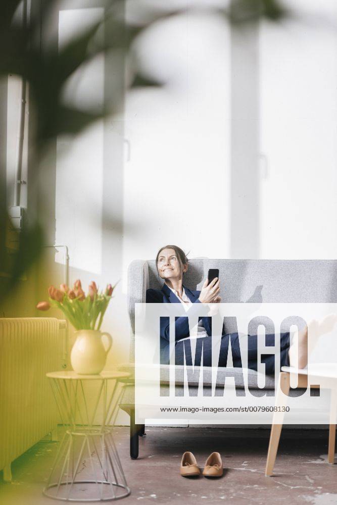 Businesswoman sitting on couch in a loft looking out of the window model released Symbolfoto property released JOSF01170
