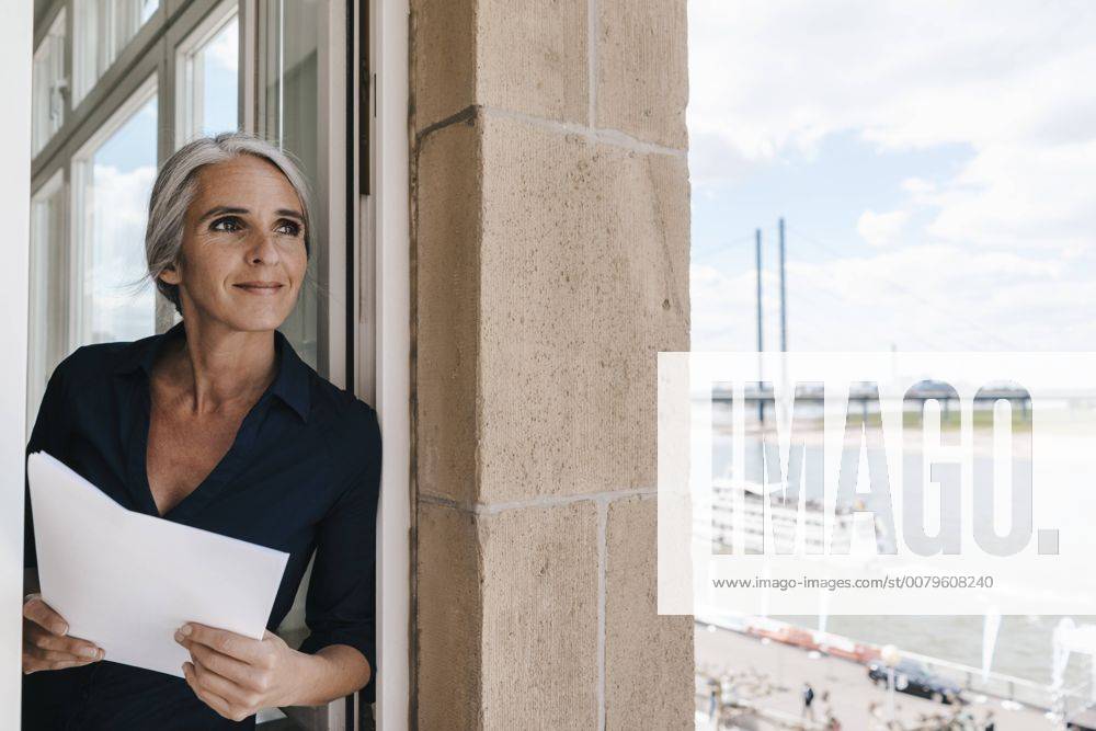 Smiling businesswoman looking out of window in waterfront office model released Symbolfoto property released KNSF01771