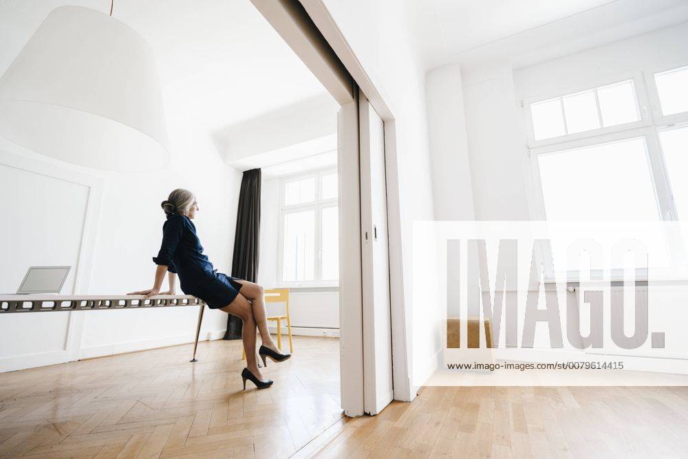 Businesswoman sitting on table in modern office model released Symbolfoto property released KNSF01808