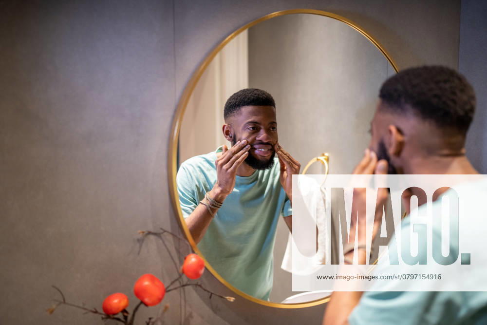 Junger afroamerikanischer Mann untersucht nach kosmetischen Eingriffen die Haut im Spiegel. Männer Derma-Pflege Junger afroamerikanischer Mann untersucht nach kosmetischen Eingriffen die Haut im Spiegel. Männer Derma-Pflege ,model released, Symbolfoto