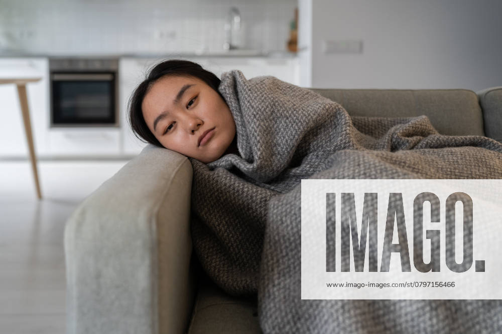 IMAGO Creative, Gesellschaft, Leisure Sickness Ungesunde, traurige, asiatische Frau, die sich kalt fühlt und mit Plaid bedeckt auf dem Sofa liegt und Depressionen durchmacht Ungesunde, traurige, asiatische Frau, die sich kalt fühlt und mit Plaid bedeckt auf dem Sofa liegt und Depressionen durchmacht ,model released, Symbolfoto