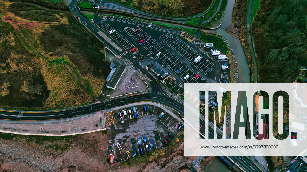 Luftaufnahme des Parkplatzes an der Küste, der Boote und des Flusses in Saltburn by the Sea Aerial view of a coastal parking area with cars, boats, and a small river. Roads and grassy hillsides surround the parking lots. Buildings are visible near the river and parking areas in Saltburn by the Sea