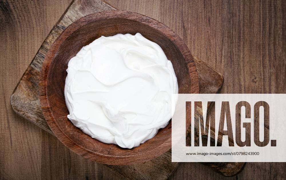 Saure Sahne in einer Holzschale, auf einem Holztisch, Draufsicht, Nahaufnahme, keine Personen Sour cream in a wooden bowl, on a wooden table, top view, close-up, no people