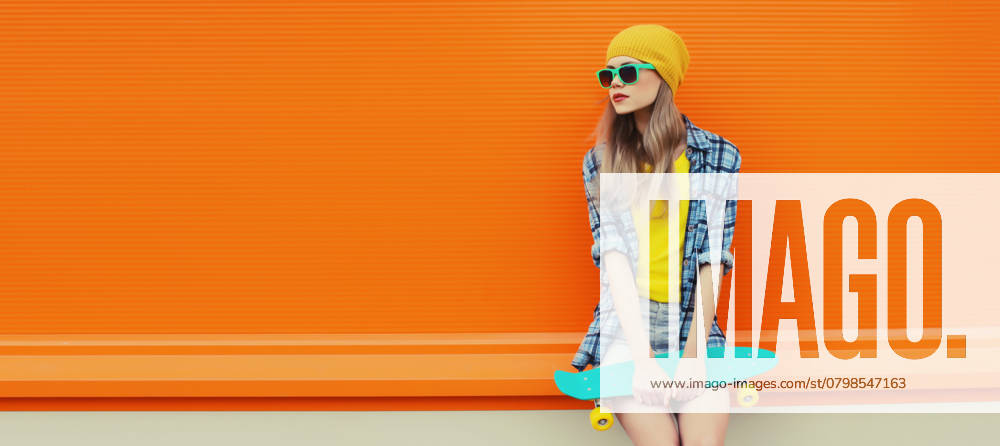 Sommer Porträt der stilvollen jungen Frau mit Skateboard in bunte Kleidung auf orange Hintergrund Summer portrait of stylish young woman with skateboard in colorful clothes, yellow hat looking away posing on orange background, blank copy space ,model released, Symbolfoto