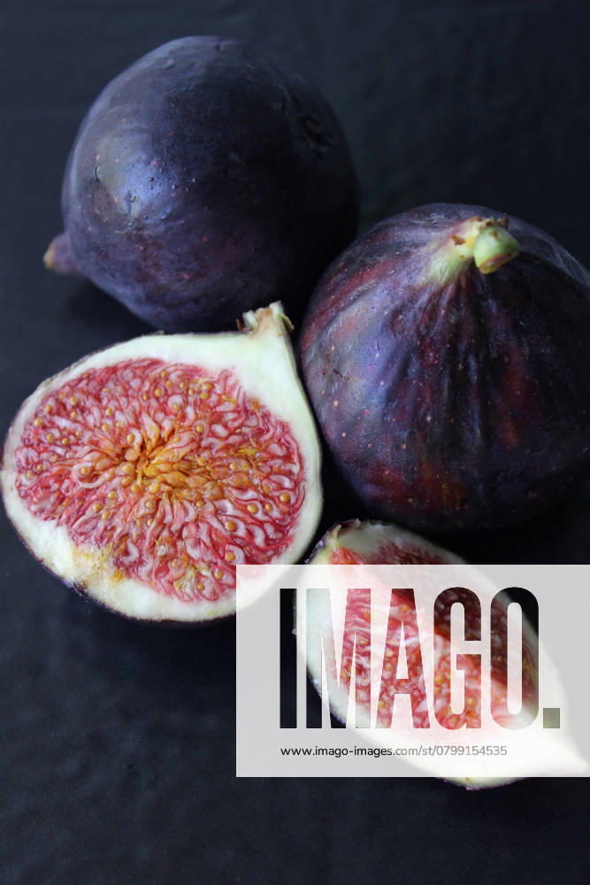 Frische Feigen mit leuchtend rotem Inneren auf dunklem Hintergrund Ripe figs, whole and cut, showcasing their vibrant red interior and seeds against a dark backdrop
