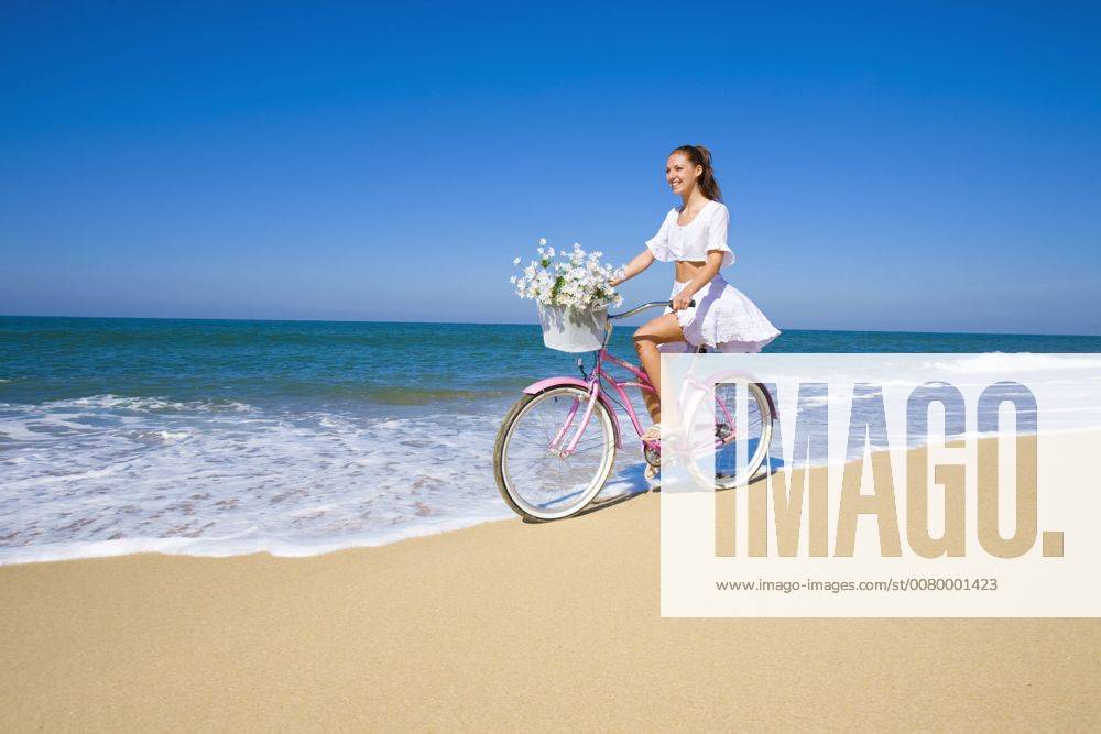 Young woman wearing a white dress riding her bike on the beach A5