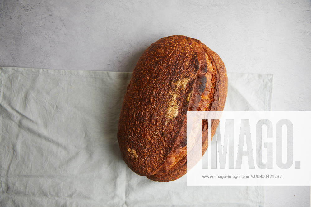 Top view of a freshly baked sourdough bread with a crispy crust, resting on a white linen cloth, offering a perfect example of traditional home baking. Model Released TwoInspirations_ID26492_764450_007