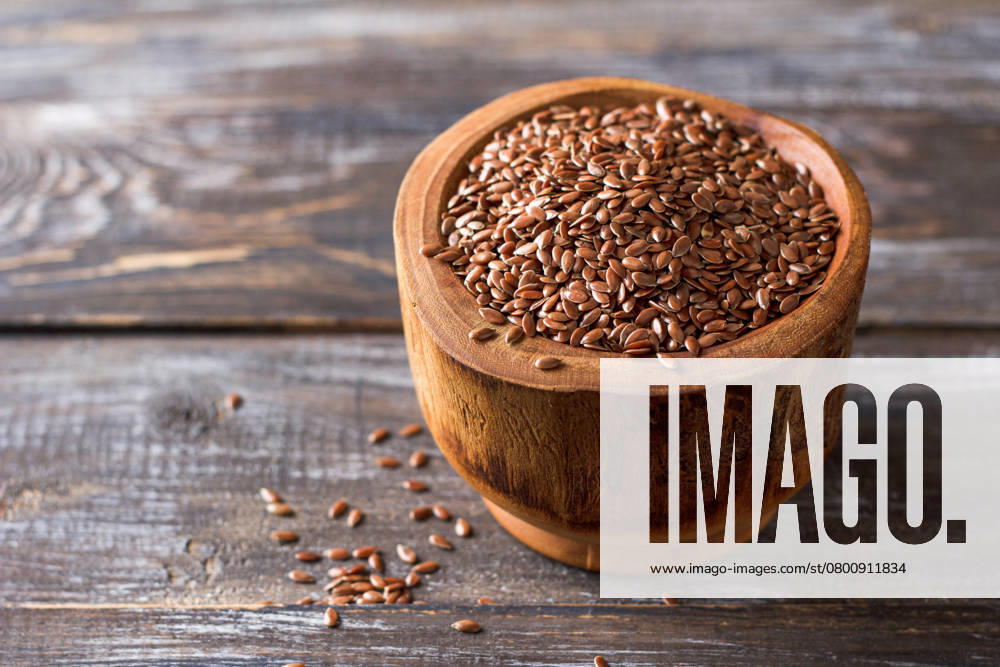 Leinsamen in einer rustikalen Holzschale auf einem Holztisch mit Kopierfläche Flax seeds in a rustic wooden bowl on a wooden table with copy space. Close-up shot of brown flax seeds in a natural wooden bowl placed on a vintage wooden surface. Warm, earthy tones with soft natural light. The background is blurred, leaving ample room for text