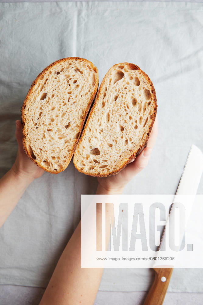 Top view of cropped unrecognizable person s hands holding fresh homemade sourdough bread halves, showcasing the airy texture and golden crust, accompanied by a bread knife on the side. Model Released TwoInspirations_ID26492_764451_008