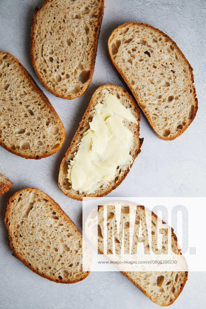 Top view of sliced fresh homemade sourdough bread with some slices generously spread with butter, set on a grey textured surface. Model Released TwoInspirations_ID26492_764459_013