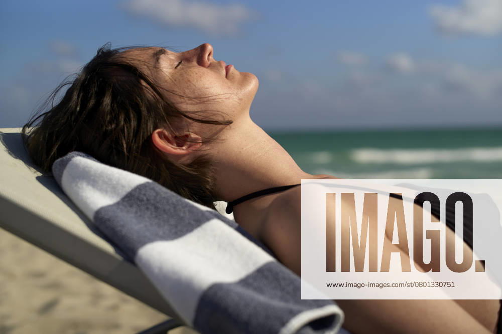 Woman in a bikini sunbathing on a beach chair by the ocean under a clear blue sky. Miami Florida USA bola06705
