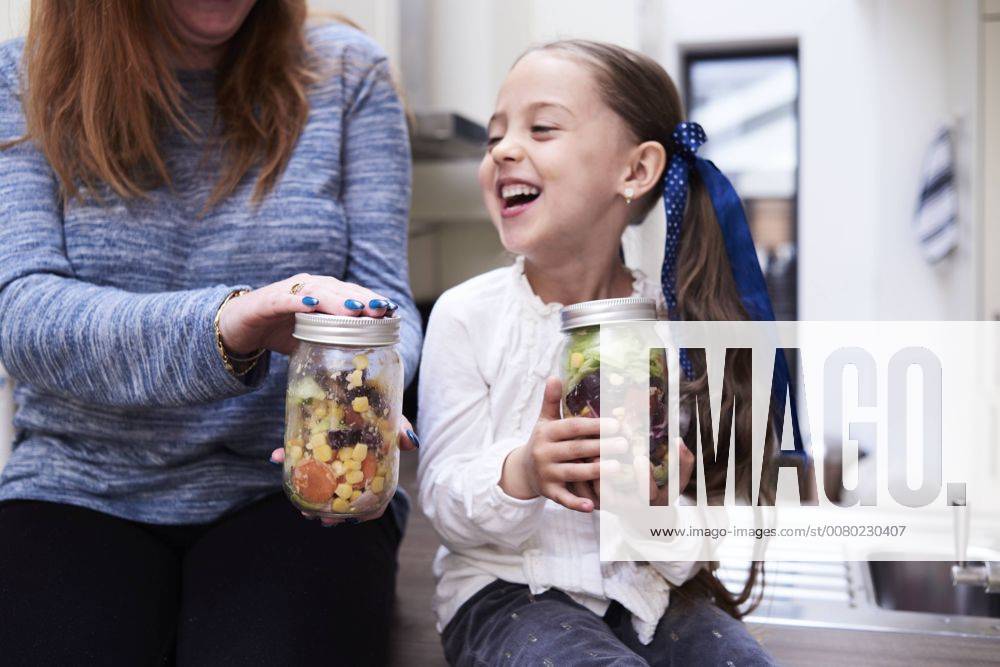 Laughing little girl with preserving jar of mixed salad sitting beside her mother model released Symbolfoto property released IGGF00005