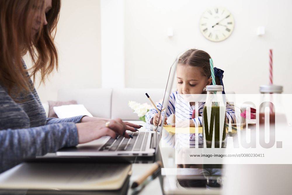 Little girl drawing with pencil at table beside her mother typing on keyboard of laptop model released Symbolfoto property released IGGF00011