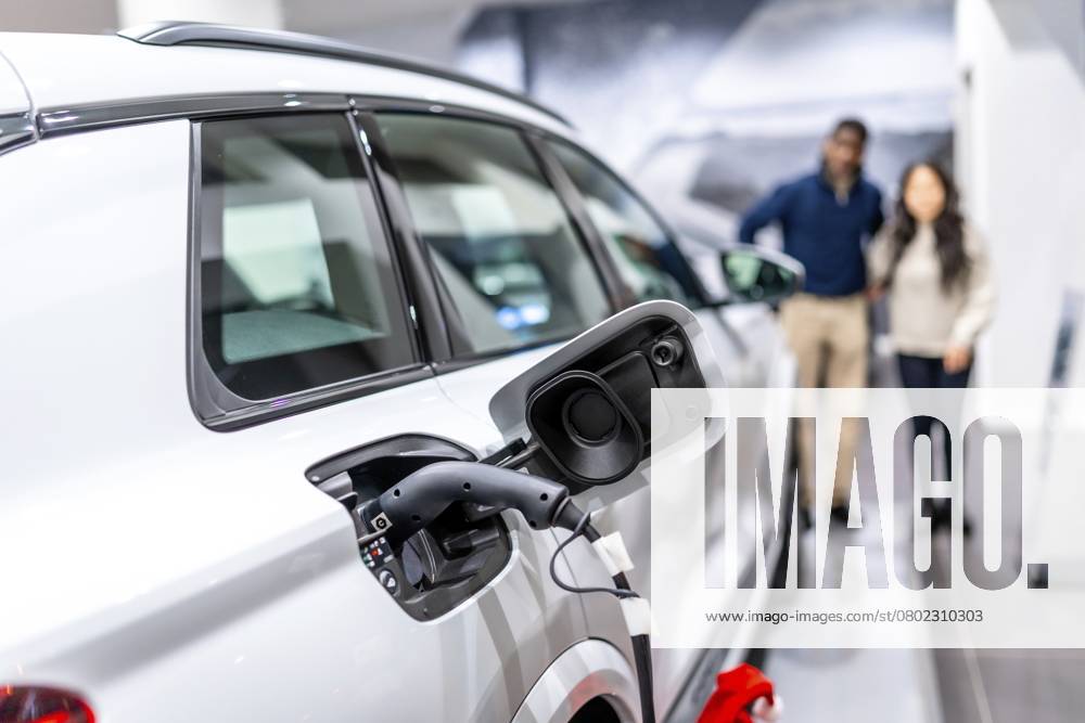 Ein Ehepaar betrachtet ein aufladbares Elektroauto in einem Autohaus und setzt auf nachhaltige Mobilität Couple looking at a charging electric car in a dealership, embracing sustainable transportation