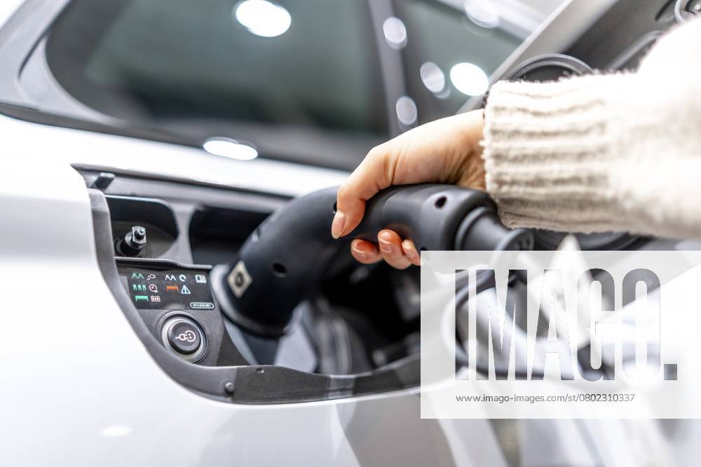 Nahaufnahme einer Hand, die in einem Autohaus ein Ladekabel an ein Elektrofahrzeug anschließt, um den Übergang zu nachhaltigen Verkehrsmitteln zu verdeutlichen Close up of a hand plugging a charging cable into an electric vehicle at a car dealership, showcasing the transition to sustainable transportation
