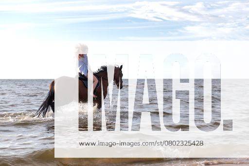 A beautiful young woman riding her horse through the water on a sunny beach 22396956 ,model released, Symbolfoto RECORD DATE NOT STATED