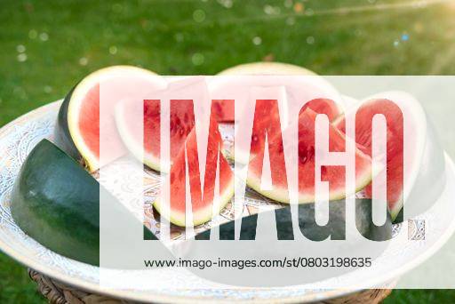 Melons pieces that look like ships lie on an African wooden tray. The melons are standing on green summer meadow with sunshine. 24394623 RECORD DATE NOT STATED