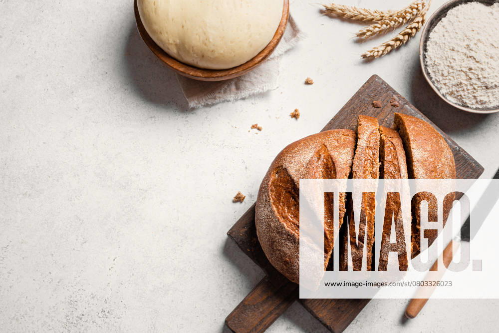Frisch geschnittenes Brot und Zutaten. Brot backen. Fresh sourdough bread and ingredients. sliced loaf of bread on cutting board, yeast dough and flour on white table, baking background, copy space, top view.