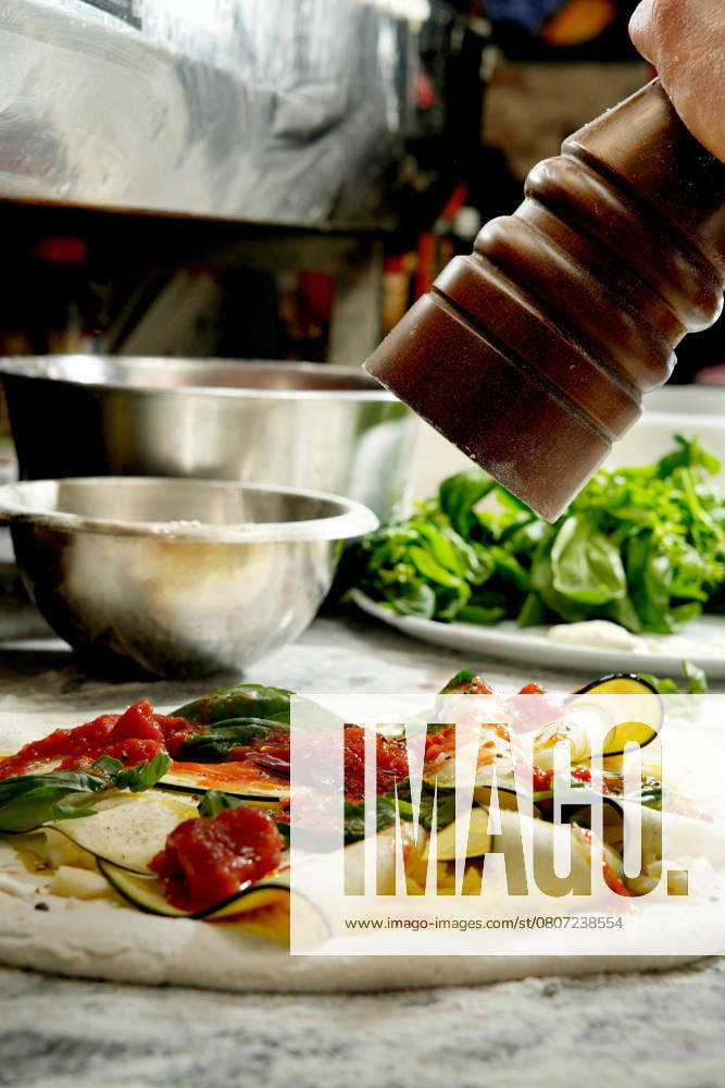 Cropped unrecognizable person seasons an uncooked pizza laden with fresh vegetables and cheese, enhancing the flavors before baking. Model Released DondykRiga_ID26863_775432_022