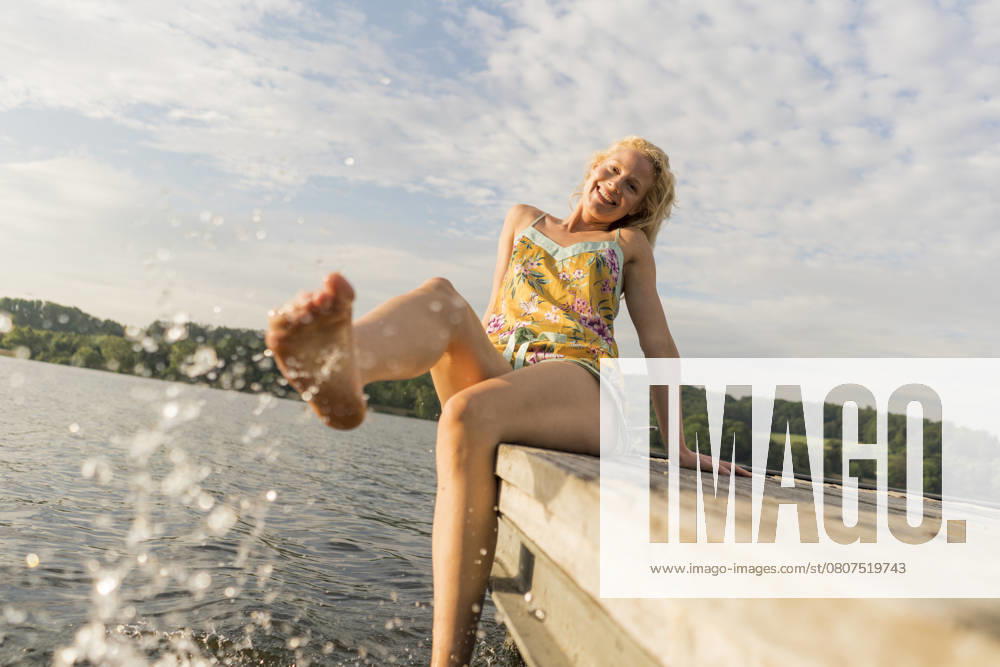 Young woman sitting on a jetty at a lake with feet in water model released, Symbolfoto, JOSF03598