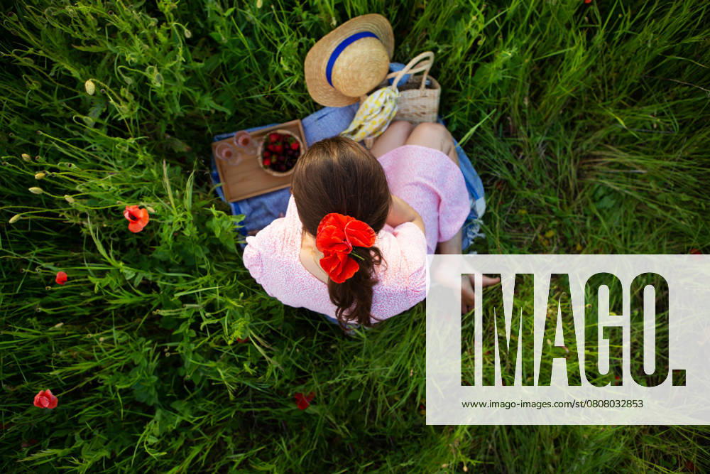 Eine junge Frau genießt ein ruhiges Picknick inmitten eines leuchtenden Mohnfeldes, umgeben von der Schönheit der Natur A young woman enjoys a tranquil picnic amidst a vibrant poppy field, surrounded by nature s beauty. ,model released, Symbolfoto