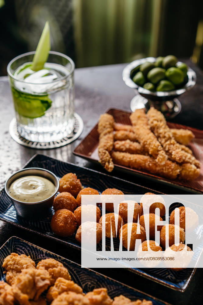 IMAGO Creative, Food, Tapas A variety of tapas featuring fried shrimp and golden-brown bites, complemented by a refreshing cocktail with lime garnishes. Perfect for a cozy dining experience. Model Released Andrerako_ID26660_769220_023
