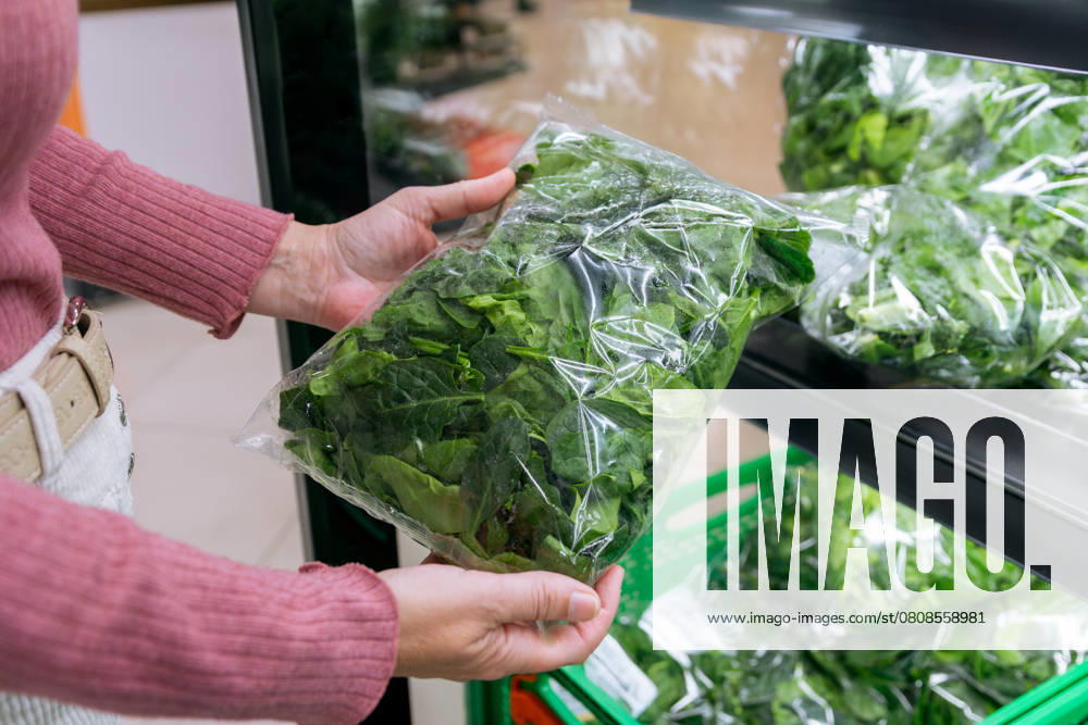 MR_ID27642_20377_RuthAlejo.jpg A woman is holding a bag of fresh spinach in a grocery store. The produce is neatly packaged and displayed on a shelf, showcasing freshness and convenience. Model Released GemaAlejo_ID27642_793910_028