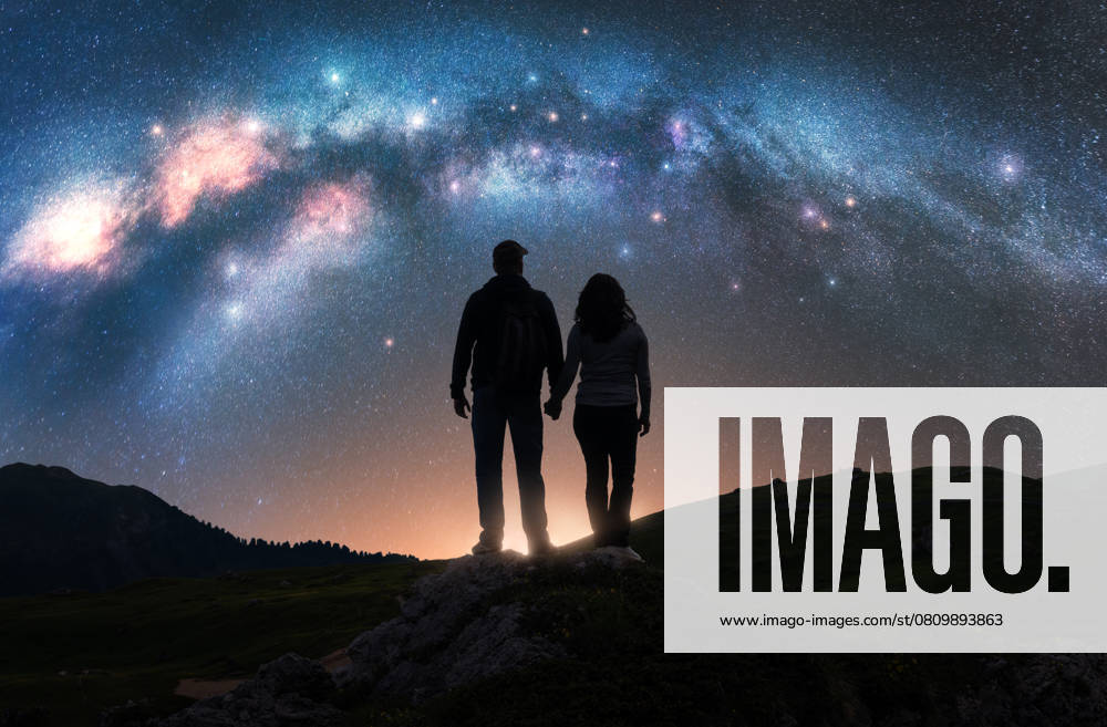 Ï¿½ouple of hikers holding hands standing on a rocky outcrop in mountains, under night starry sky with glowing Milky Way. Colorful landscape with silhouettes of man and woman, bright stars and milky way Model Released DenisBilytskyi_ID27418_786785_014