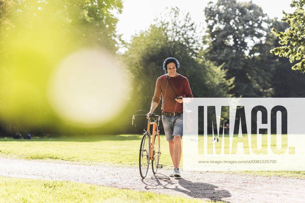 Man with racing cycle listening music with headphones in a park model released Symbolfoto UUF11740