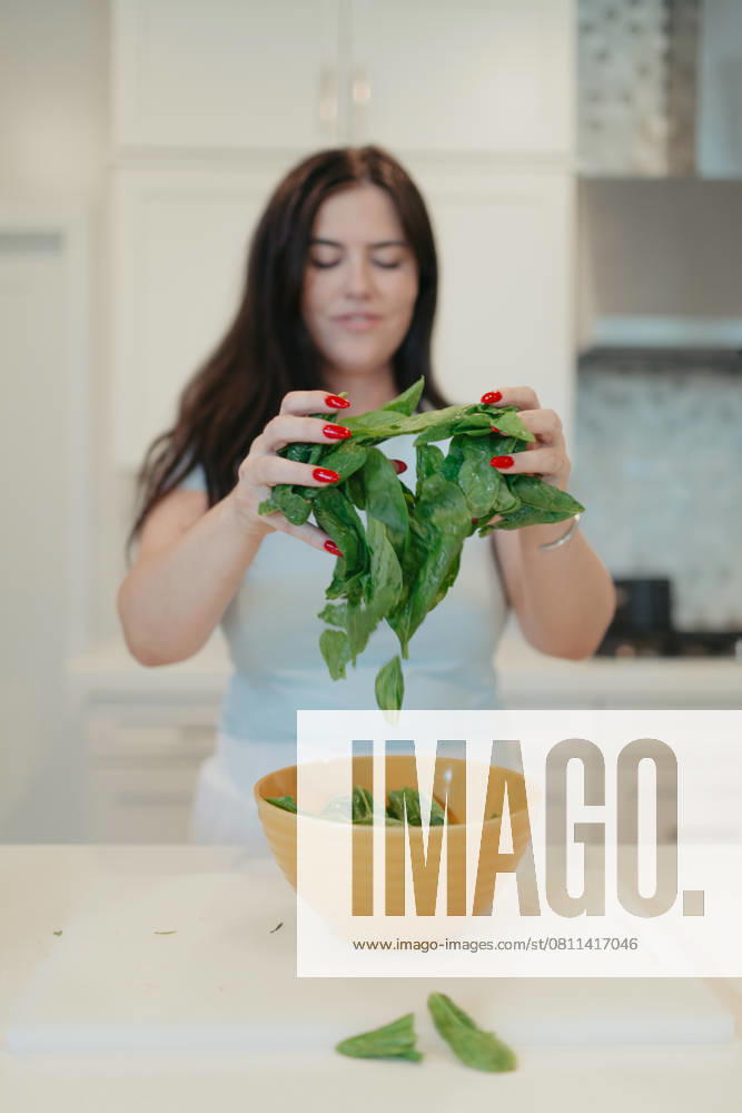 Woman adding fresh spinach leaves into a yellow bowl. Vista, California, United States R_AUAU250409B-1700357-01 ,model released, Symbolfoto ,property released