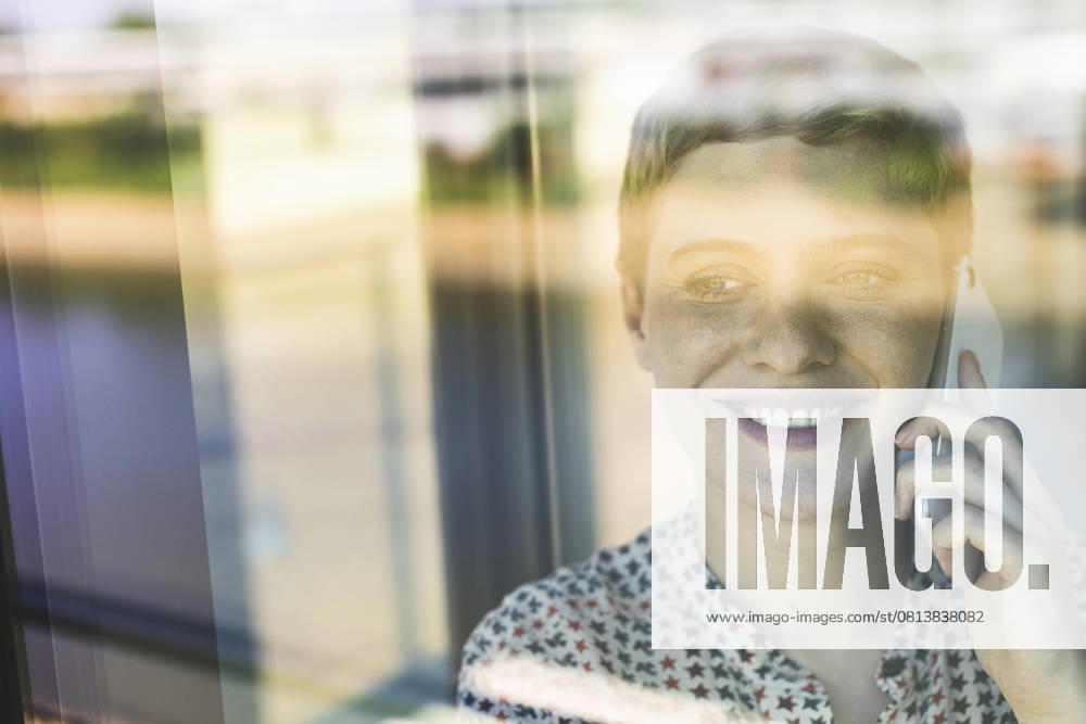Close-up of smiling businesswoman talking over smart phone in office seen through window model released, Symbolfoto property released, UUF21521