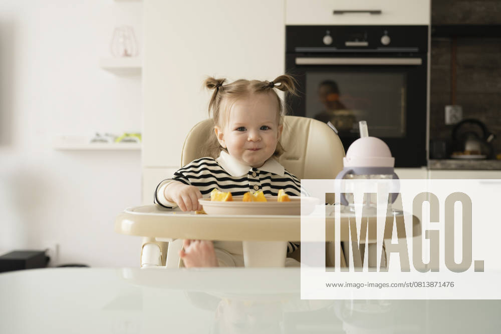 Toddler in a kitchen eating at a high chair with a striped shirt and pigtails model released, Symbolfoto property released, LESF00673