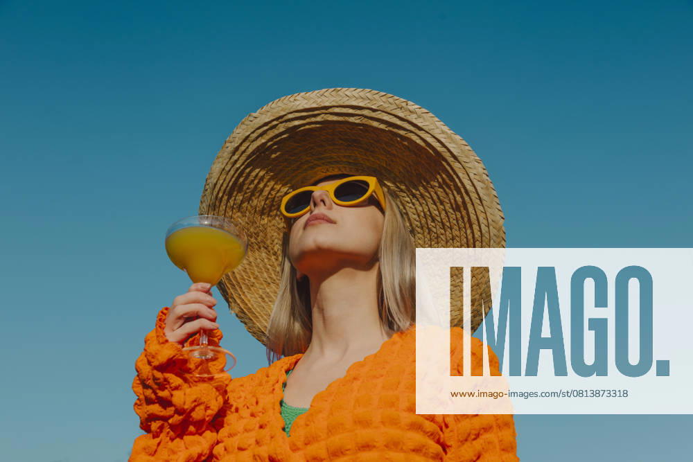 Stylish woman in orange clothing and straw hat enjoying a cocktail outdoors model released, Symbolfoto, VSNF03025