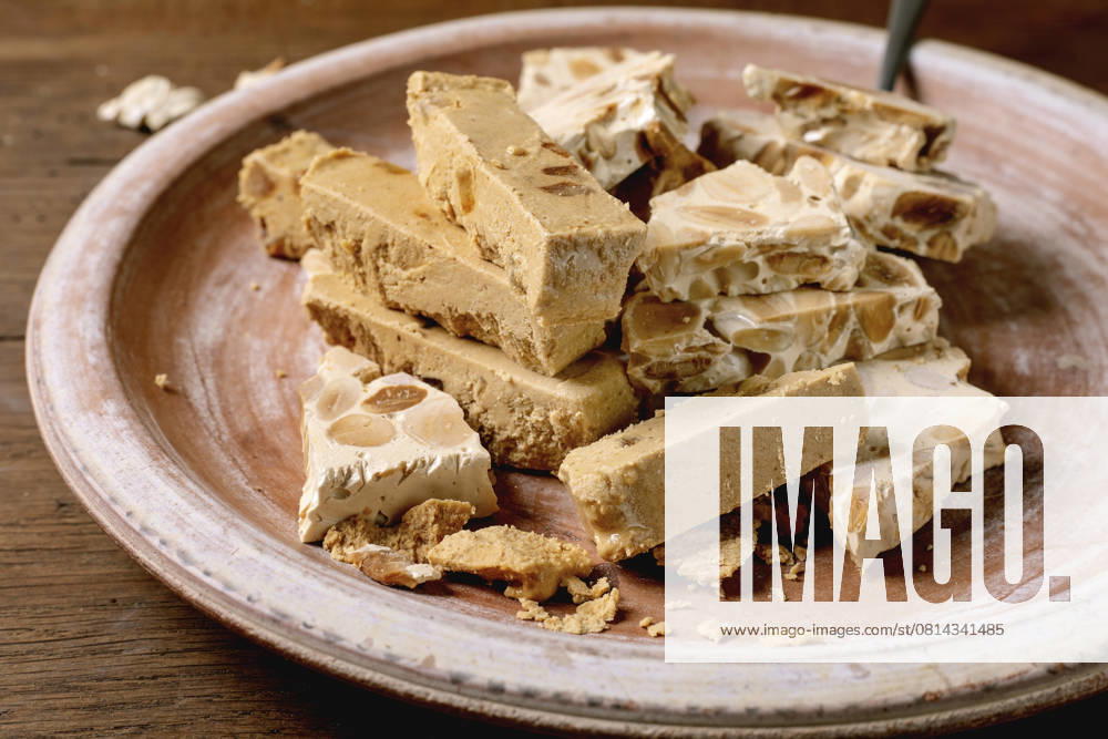 Spanish dessert classic turron Traditional Spanish dessert classic soft orange turron and crunchy almond turron, cut into pieces on rustic clay plate with fork. Wooden table, top view.