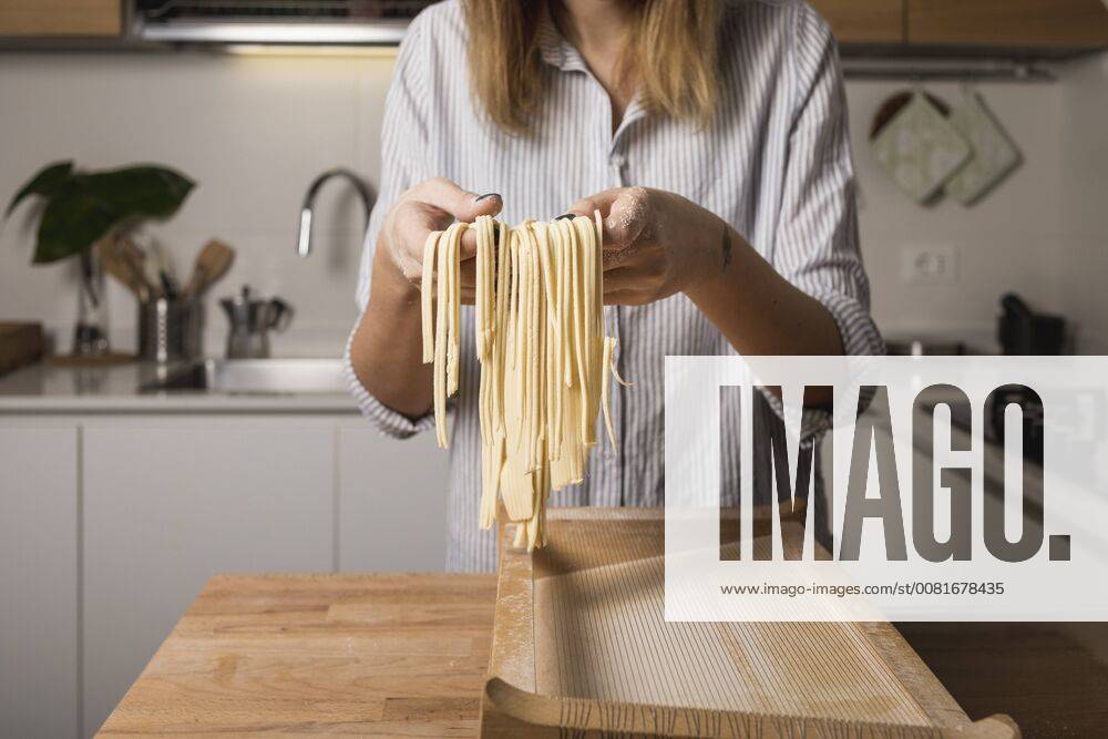 Woman preparing homemade pasta, holding row noodles, pasta harp model released Symbolfoto property released MAUF01262