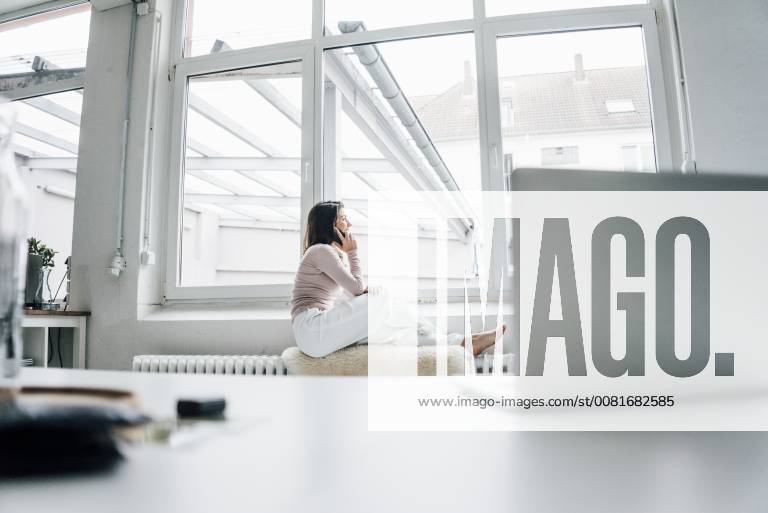 Young woman on the phone sitting on sheepskin on heater in a loft looking out of window model released Symbolfoto property released MOEF00446
