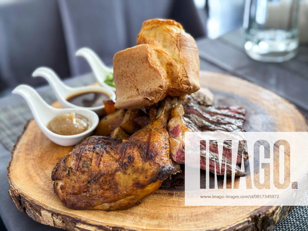 A succulent plate of steak slices and roasted chicken leg served with Yorkshire pudding and a trio of delicious sauces, presented on a rustic wooden board on a cafe in Thailand Model Released IrinaChetverikova_ID28328_834977_006