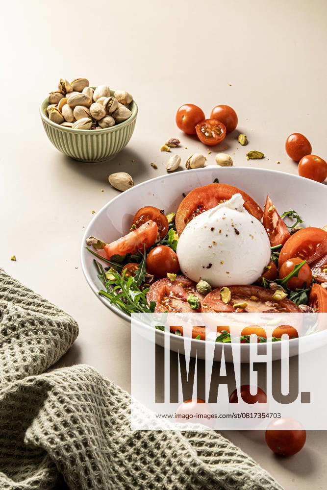 A vibrant salad featuring creamy burrata, juicy tomatoes, and crunchy pistachios. Served in a white bowl with a fresh texture, perfect for a nutritious meal experience. Model Released StudioMostaza_ID28208_830854_004