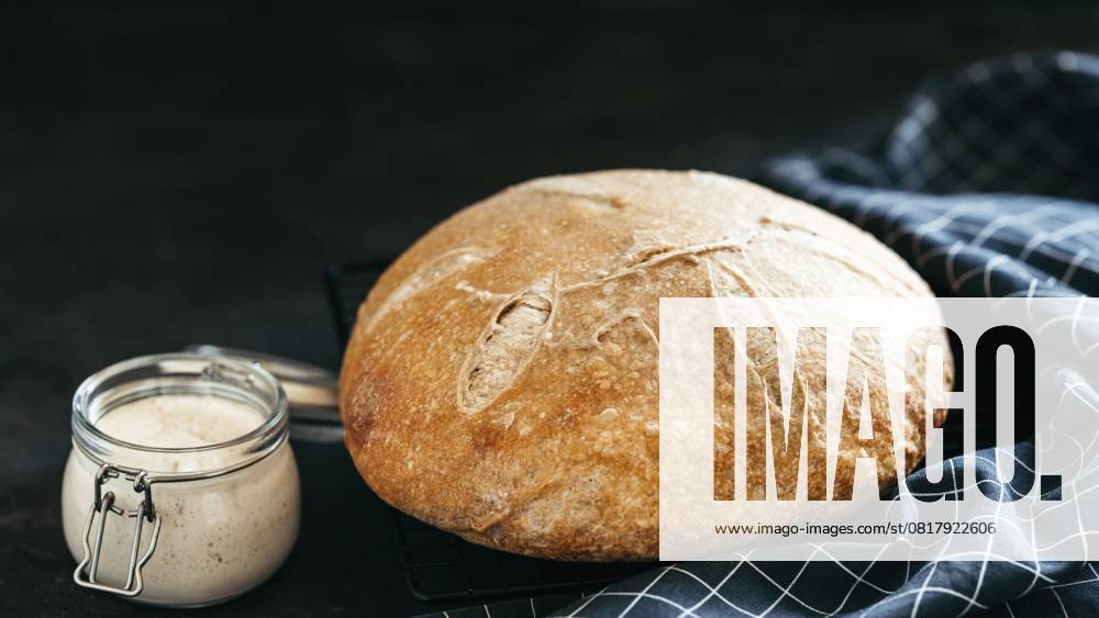 Weizen runden Sauerteig Brot und Sauerteig Starter in Glas jar.Side Ansicht von hausgemachten Sauerteig Brot auf schwarzem Hintergrund mit Kopie Raum. Lange horizontale banner.Home gemacht Sauerteig Brot machen Konzept Wheat round sourdough bread and sourdoug starter in glass jar.Side view of homemade sourdough bread on black background with copy space. Long horizontal banner.Home made sourdough bread making concept