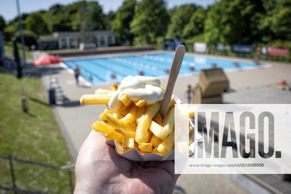 Outdoor pool fries Fresh fries with mayonnaise in a typical white cardboard bowl are held by a hand in t