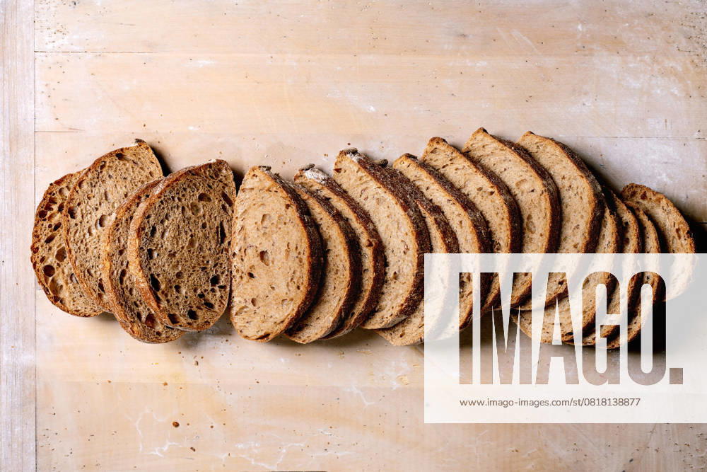Geschnittenes Handwerks-Sauerteigbrot Laib Freshly baked artisan sourdough bread sliced into portions on wooden background. Crusty rustic loaf with airy texture shows natural fermentation pattern. (License=RF)