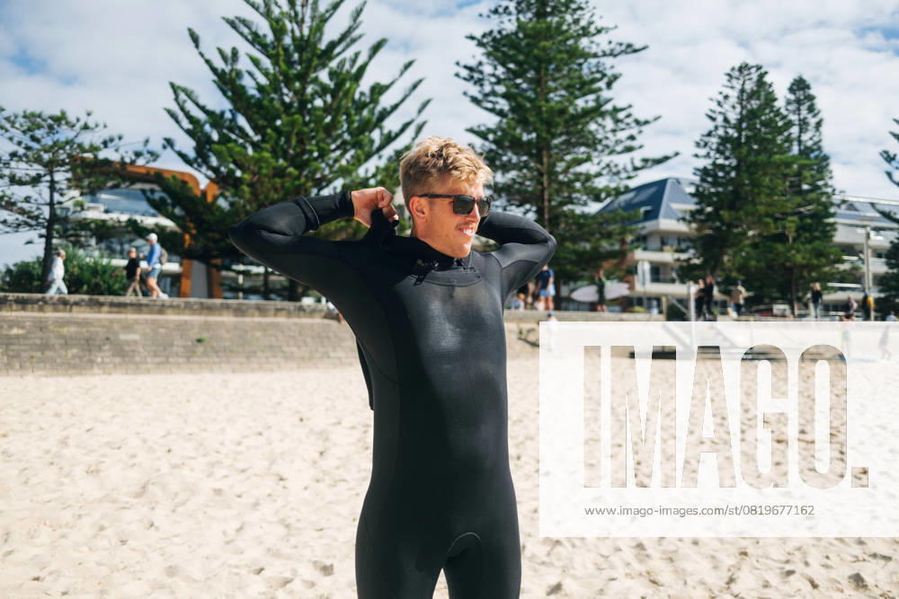 Man in wetsuit smiling on sunny beach near modern buildings Manly, New South Wales, Australia CR_MGTP250515B-1727293-01 ,model released, Symbolfoto