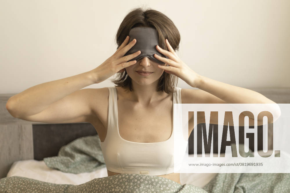 Young woman wearing a sleep mask on bed holding hands near her eyes R_DCGM250515-1732425-01 ,model released, Symbolfoto