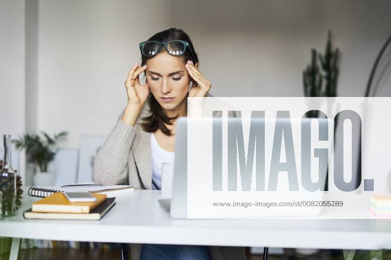 Young woman at home with laptop on desk touching her temples model released Symbolfoto property released BSZF00168