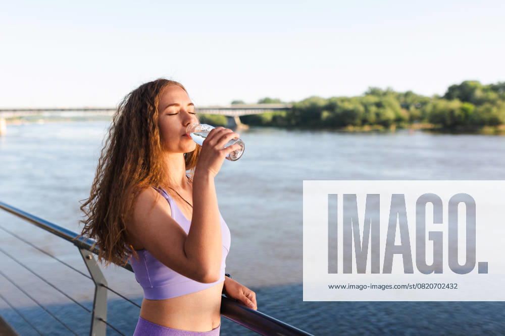 Sporty woman drinking water in activewear by river Warsaw, Masovian Voivodeship, Poland R_NAJJ250523-1736437-01 ,model released, Symbolfoto